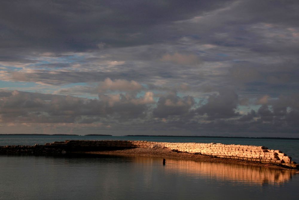 A man swims next to a manmade wall built to protect the island of South Tarawa from rising tides in the central Pacific island nation of Kiribati May 25, 2013.