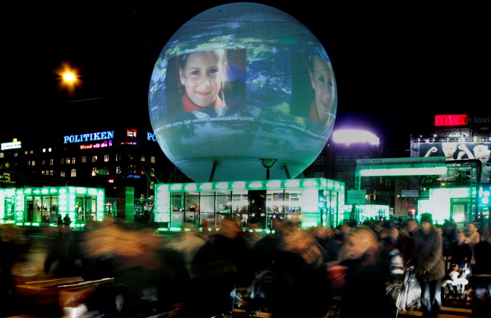 image with buildings with green lights in windows and a large globe-like item with images projected on it.