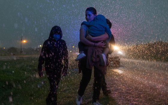 A mother from Central America and her three children are followed by a Texas Highway Patrol officer in La Joya, Texas, May 19, 2021, as they look for cover during a heavy rainfall after crossing the Rio Grande into the United States from Mexico. (CNS)