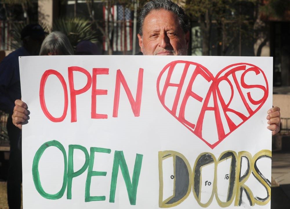 Man holds sign that reads, "Open hearts/open doors."