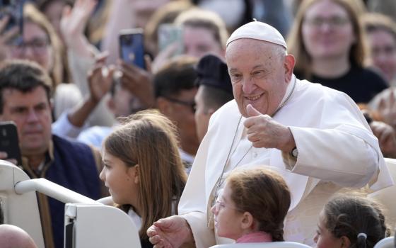 Francis seated in popemobile, smiles and gives thumbs up.