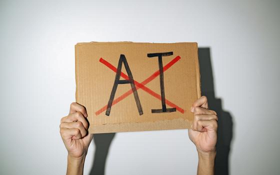 Hands holding a cardboard sign with the letters AI crossed out (Dreamstime/Wachiwit)