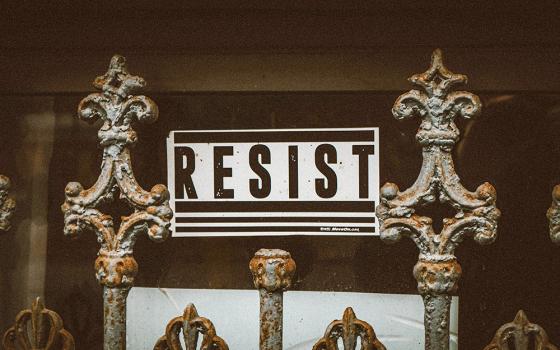 Sign behind a gate says, "RESIST" (Unsplash/Jon Tyson)