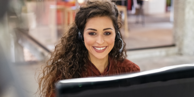 Woman customer operator with headset working on computer. Portrait of young sales agent in conversation with customer over headset at office. Friendly call center agent working on support online.